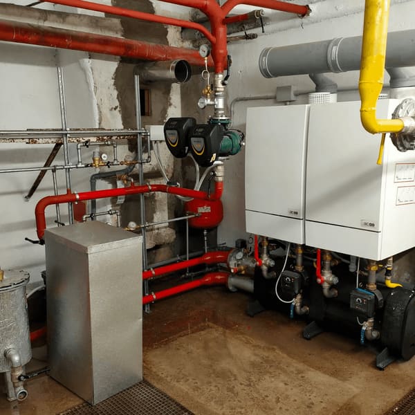 Centrale termica condominiale con tubazioni rosse, caldaie a parete e pompe di circolazione